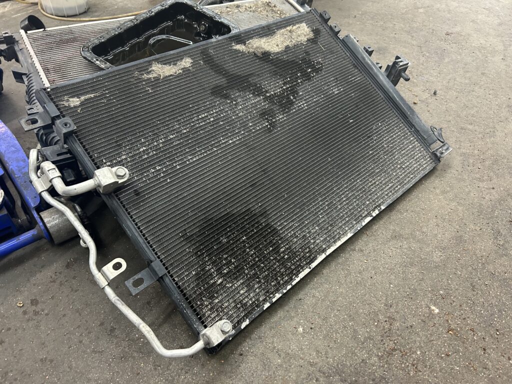 Used, dirty car radiator with visible debris and coolant stains on a shop floor, removed for inspection or replacement.