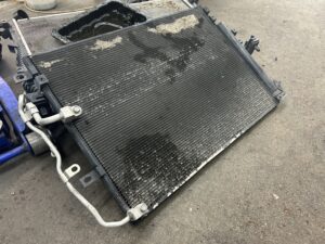 Used, dirty car radiator with visible debris and coolant stains on a shop floor, removed for inspection or replacement.