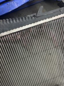 Close-up of a vehicle radiator showing signs of coolant residue and fin corrosion near the upper plastic tank.