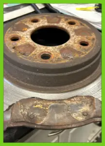 Rusty brake drum and worn-out brake shoe on a workbench during a vehicle brake service.