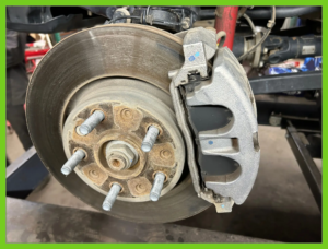 Close-up of a vehicle's front disc brake assembly showing the brake rotor, caliper, and brake pads on a lifted Jeep.