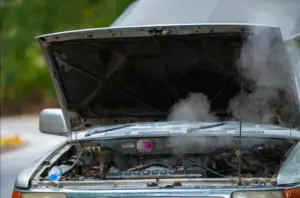 Older model vehicle on the roadside with steam escaping from the engine under an open hood.