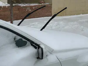 Two windshield wiper blades raised upright on a snow-covered car to prevent freezing.