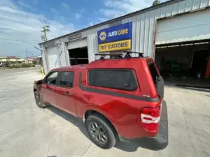 Red truck parked outside TNT Customs Auto Repair shop featuring a newly installed ARE topper with roof rack.